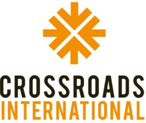 Crossroads International logo - image of four orange arrows pointing towards each other inward to form a circle, with the word crossroads in black and the word international in orange