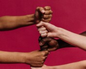 Fists of people of different backgrounds and races one on top of the other on a red background, symbolizing solidarity and unity.
