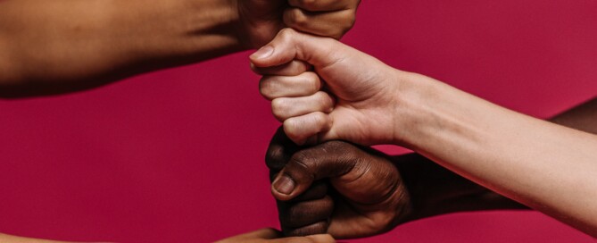 Fists of people of different backgrounds and races one on top of the other on a red background, symbolizing solidarity and unity.
