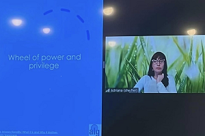 Screenshot of a woman giving a virtual presentation. The slide she is showing has text that says wheel of power and privilege with a graphic.