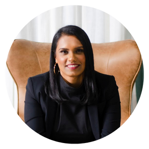 Women with dark hair and wearing a black jacket and shirt, smiling and sitting in a leather chair.