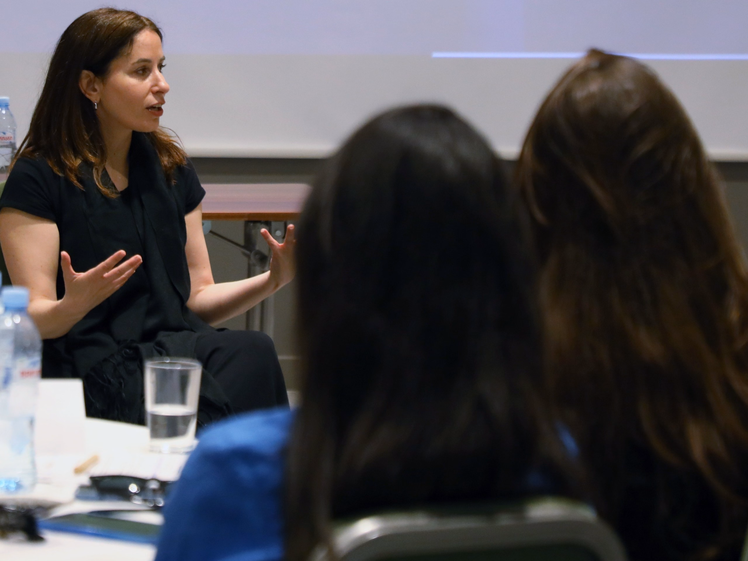 Femme (blanche et juive) avec les cheuveux bruns longs présentant un atelier à un groupe.